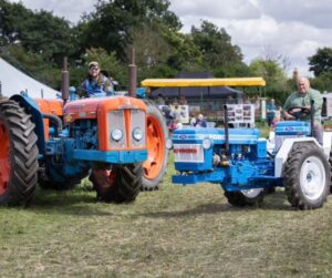 Vintage tractors side by side. one on the left is orange and blue, while the one on the right is pale blue.