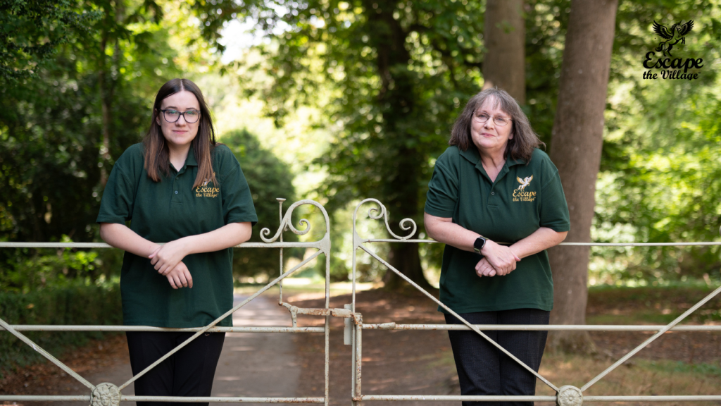 Izzy and Liz together out in the countryside, behind a crafted metal gate.